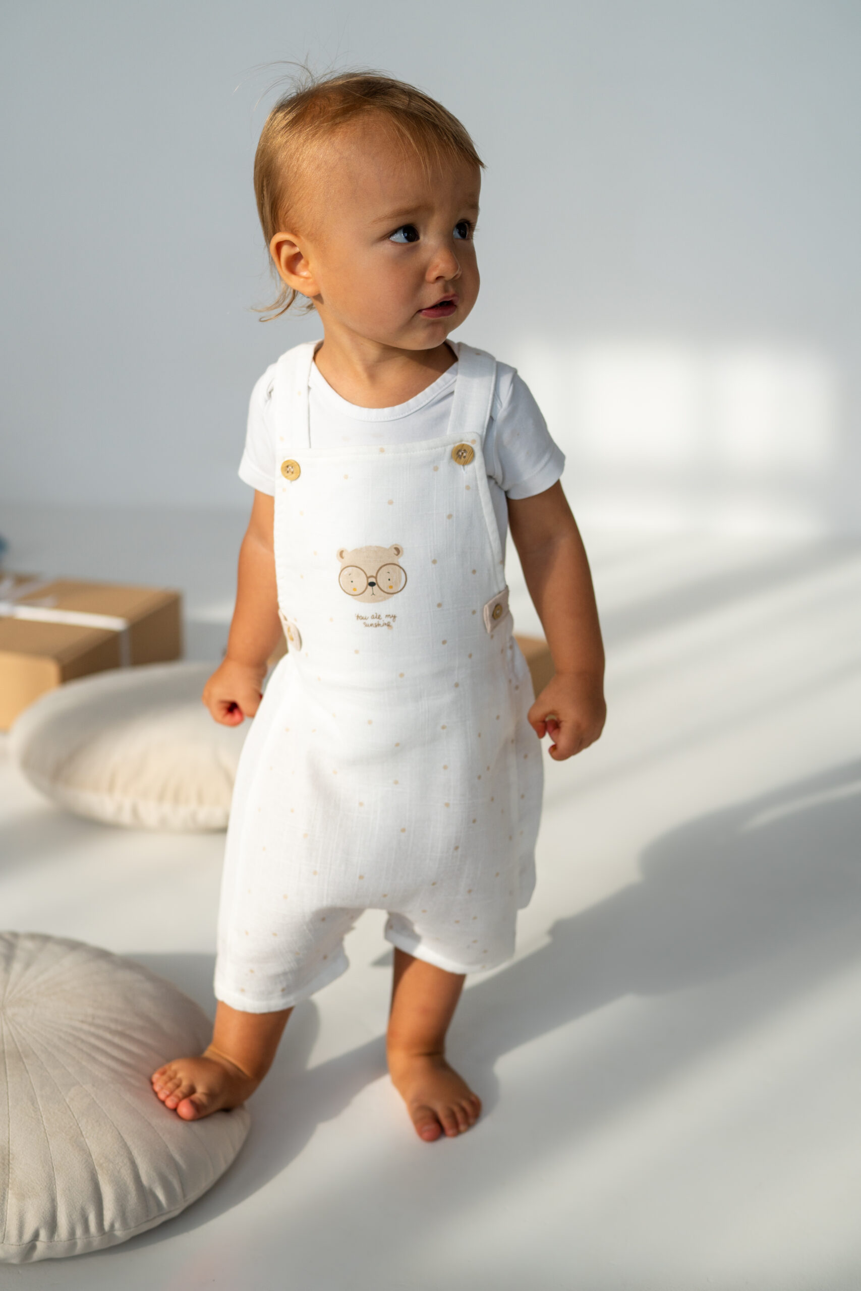 Salopetă bebeluși cu ursuleț și pălărioară cu urechi – bumbac Salopetă bebeluși crem cu bretele și imprimeu ursuleț, din bumbac moale, set cu pălărioară cu urechi, outfit drăgălaș și confortabil pentru copii