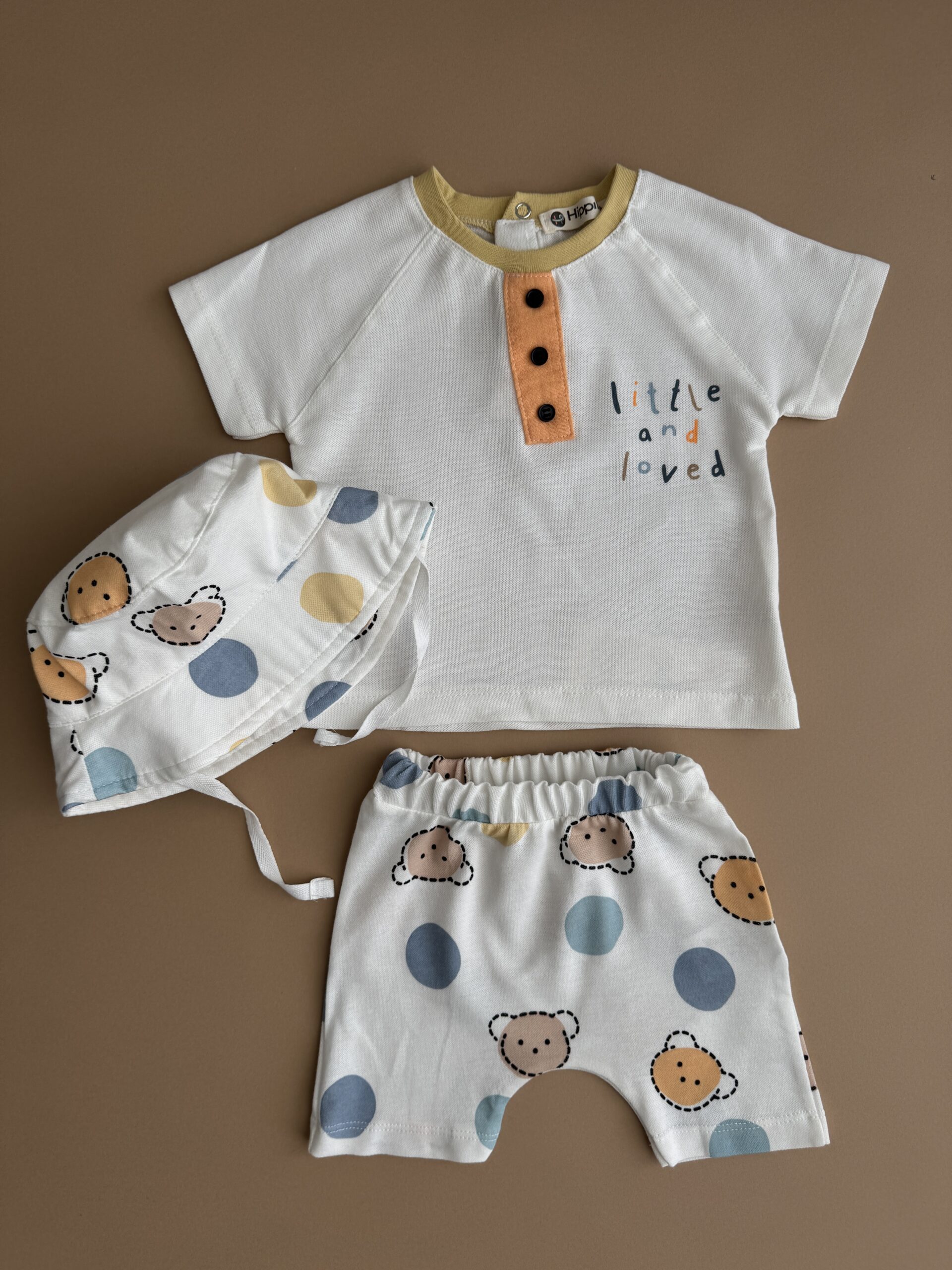 set-haine-copii-vara-bumbac Set haine copii compus din tricou alb cu nasturi, pantaloni scurți cu modele grafice și pălărie de vară din bumbac.