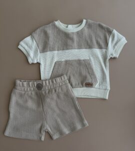 Set haine băieți bumbac format din tricou texturat bej și pantaloni scurți asortați pe fundal neutru.
