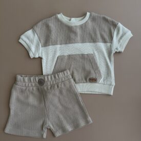 Set haine băieți bumbac format din tricou texturat bej și pantaloni scurți asortați pe fundal neutru.