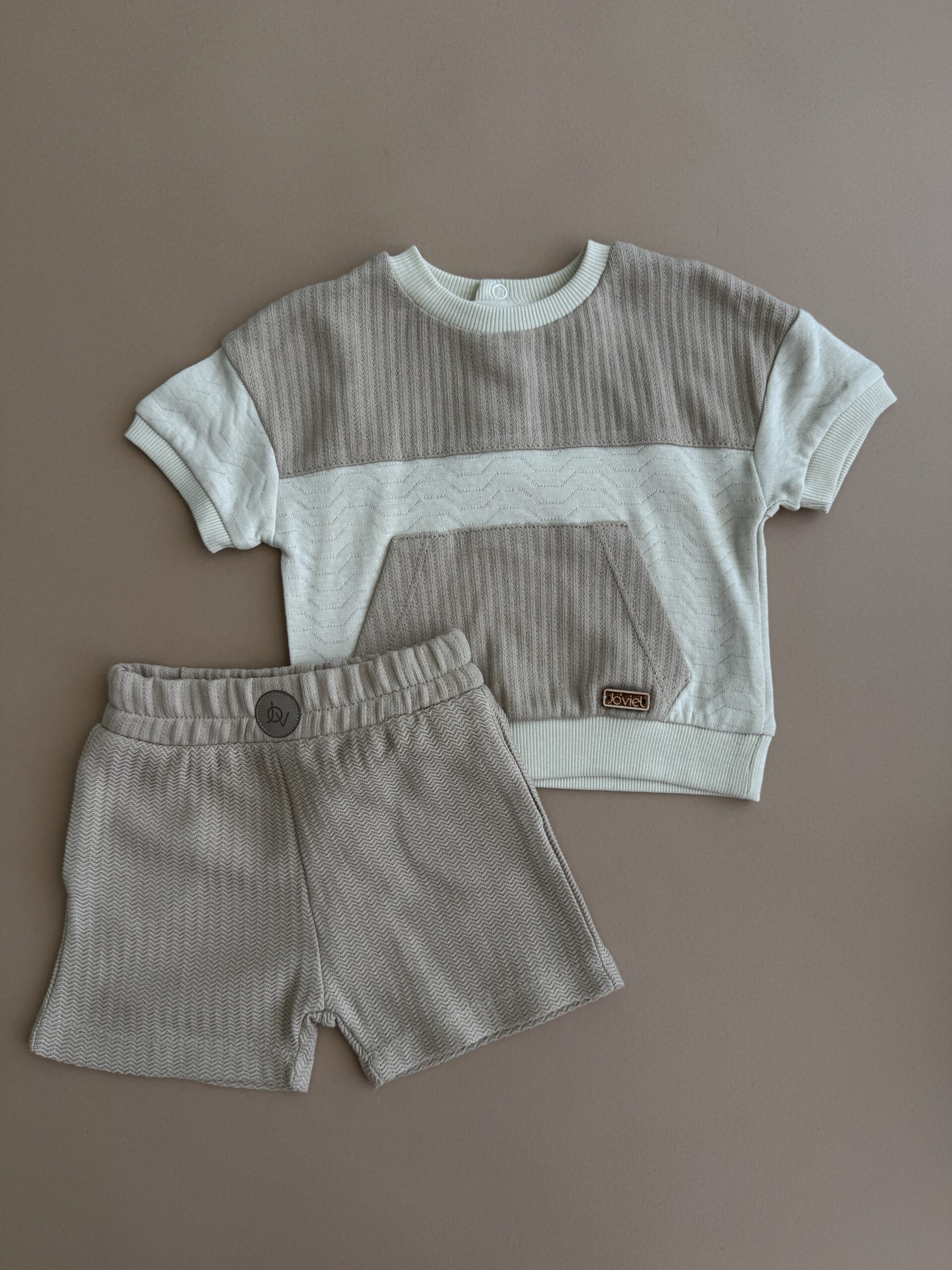 Set-premium-baieti-bumbac-bej Set haine băieți bumbac format din tricou texturat bej și pantaloni scurți asortați pe fundal neutru.