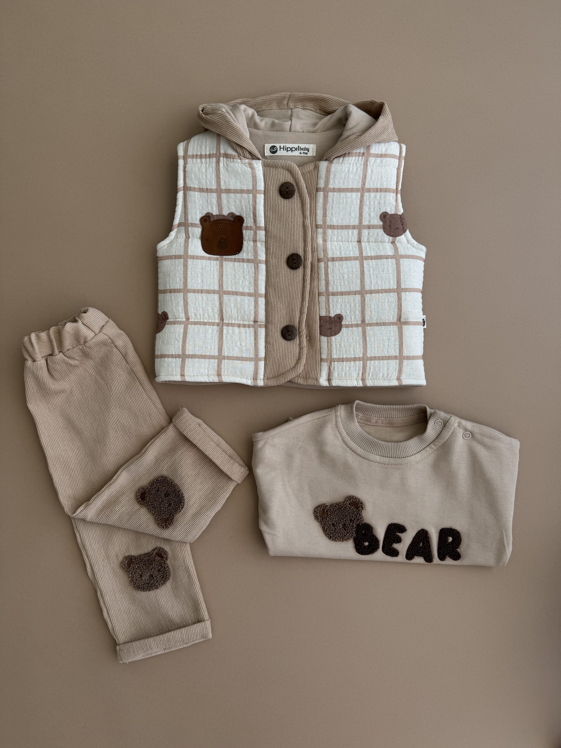 Set 3 piese cu ursuleți pentru bebeluși – vestă, bluză și pantaloni Set din 3 piese pentru bebeluși, format din vestă cu glugă și imprimeu ursuleți, bluză bej cu aplicație ‘Bear’ și pantaloni asortați, confecționate din materiale moi și confortabile – ideal pentru ținute de toamnă-iarnă