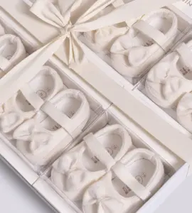 Pereche de pantofiori eleganți pentru bebeluși tip balerini cu fundiță albi și bareta elastică în cutie cadou premium.