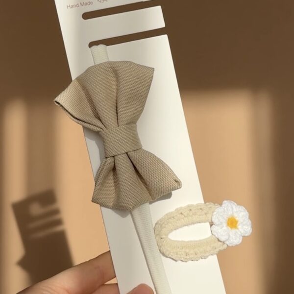 Set accesorii păr pentru bebeluși format din bentiță bej cu fundiță și agrafă crem croșetată manual cu detaliu floral.