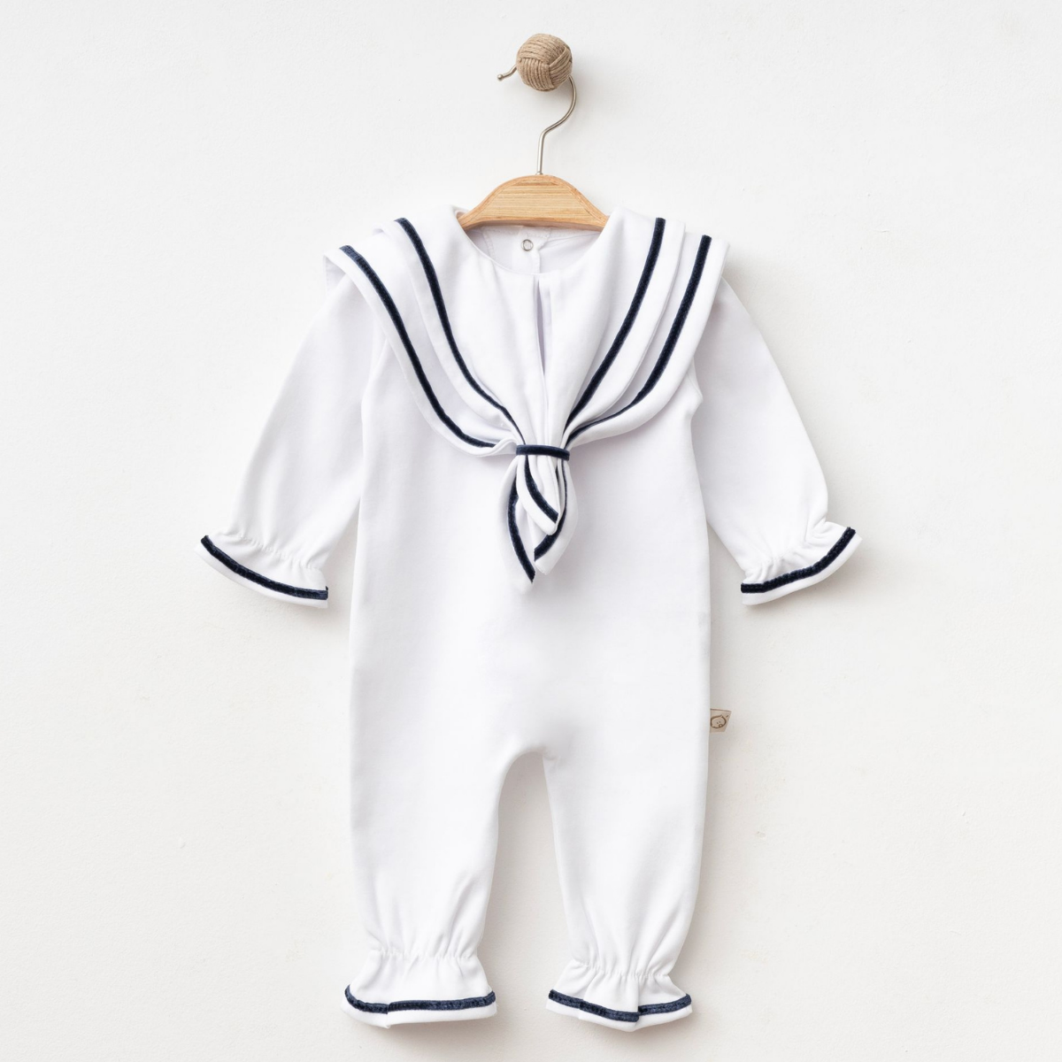 salopeta-eleganta-bebelusi-stil-marin Salopetă albă pentru bebeluși cu guler marin și margini bleumarin expusă pe umeraș de lemn.