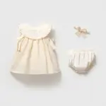 Set 3 piese pentru fetițe cu rochiță ivoriu brodată floral, chiloțel asortat și bentiță cu fundiță din dantelă pe fundal gri.