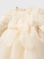 Detaliu pe bustul unei rochițe crem ivoriu pentru fetițe cu flori 3D texturate, fundă mare din organza și fustă din tul.