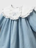 Detaliu pe gulerul dublu alb cu broderie florală albastră și volănașe al unei rochițe pentru fetițe din material albastru pastel.