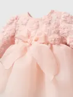 Detaliu pe bustul unei rochițe roz pudrat pentru fetițe cu flori 3D texturate, fundă mare din organza și fustă din tul.